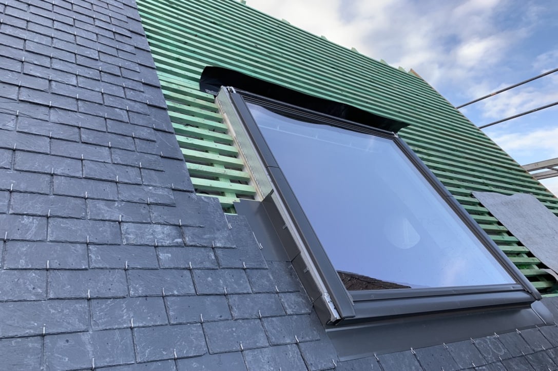 Gros plan sur la pose d'ardoise autour d'un Velux, on voit distinctement les crochets qui maintiennent les ardoises sur la toiture. C'est un travail de couverture réalisé par Monsieur bouthors.